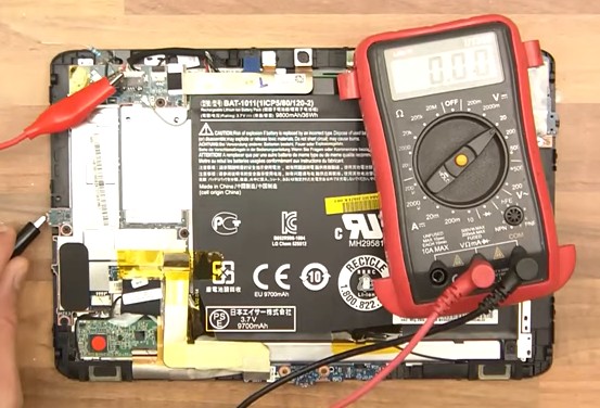 A person using a multimeter to test the tablet with a broken charging port.